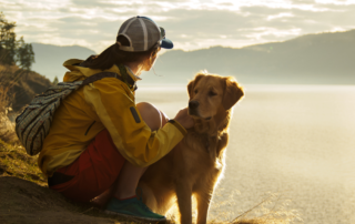 A woman and her dog enjoying the sunrise at a mountain lake